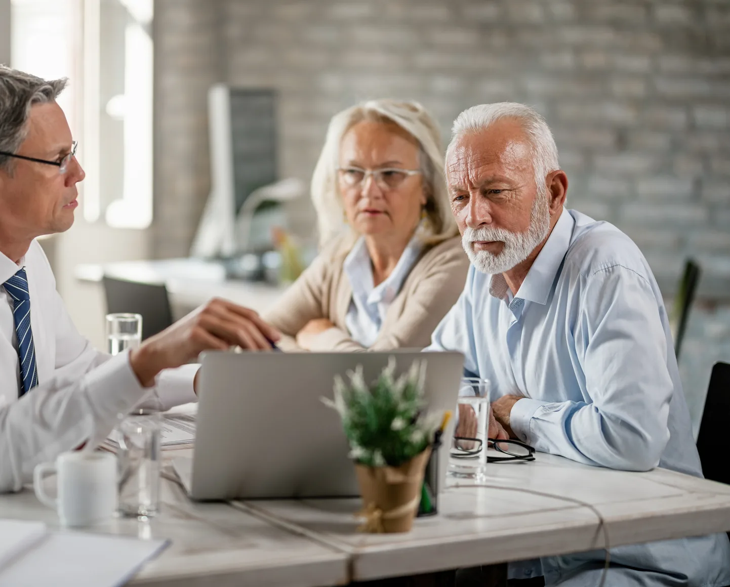 An older couple sit at an office table with their advisor, who talks them through the figures on his laptop
