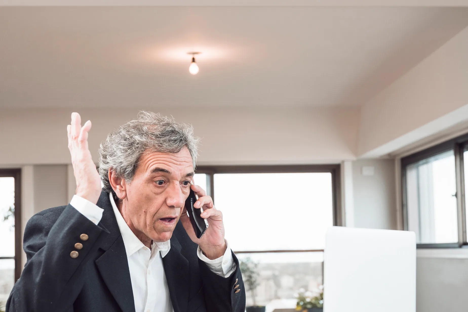An owner in a blazer talks on the phone at his desk, one hand raised mid sentence